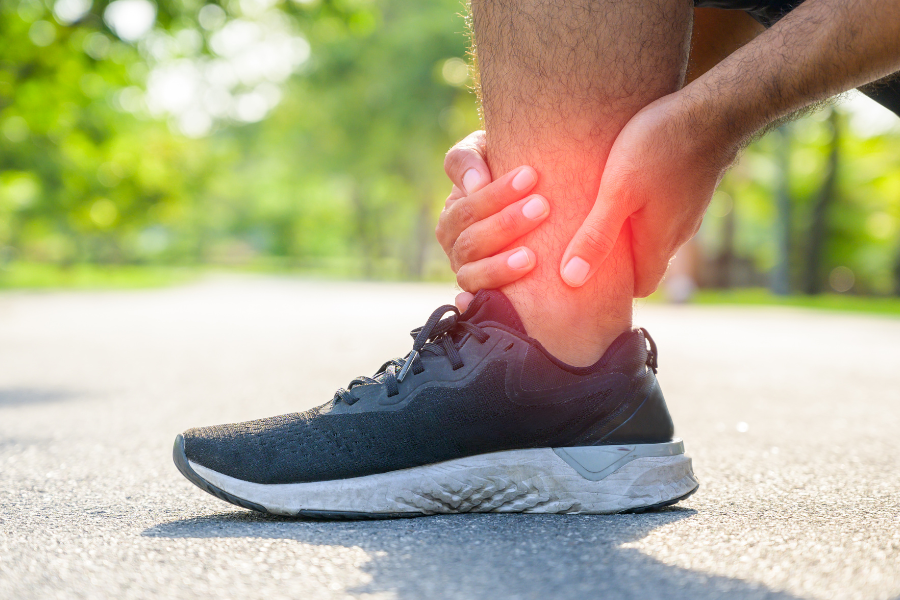 Man on running path knelt over holding hurt ankle